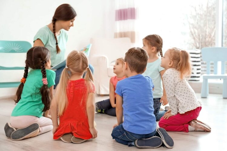 Female teacher reading book to little children in kindergarten